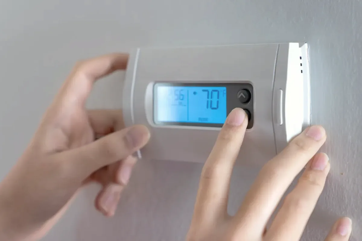 Hands adjusting a digital wall thermostat