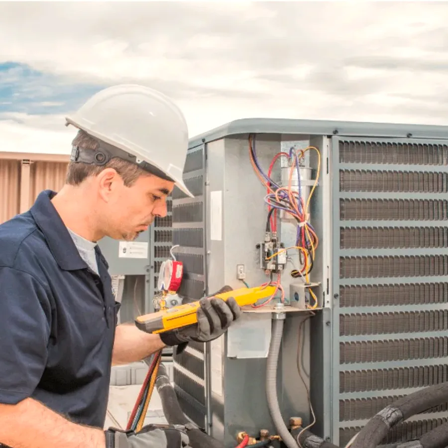 HVAC technician in a hard hat testing an outdoor air conditioner with a multimeter